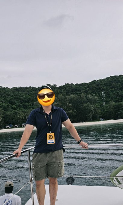A person wearing a Binance lanyard and ID badge stands on a boat during a sunny sailing trip, with ocean and lush green coastline in the background—capturing the relaxed, social atmosphere of the #BinanceCampus event.

The face is obscured by a smiley-face emoji, so no facial features are visible.