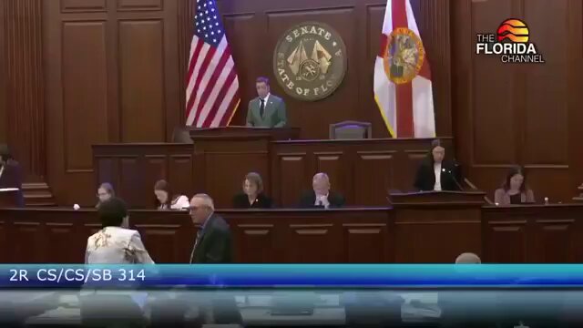 The image shows a courtroom scene where a judge sits at his desk, surrounded by people who appear to be either sitting or standing around him. The judge appears to be listening attentively as he speaks into a microphone. A news anchor can be seen in front of the judge, likely reporting on the proceedings. In the background, there are two flags - one representing the United States and another representing Florida. The image also contains text that reads "The Senate Banking Committee approved the CLARTY Act on May 14th with a 9-6 vote!! Aftersenate approval, it will go to President Trump for signature. And with this clarity provided, XRP could be the asset that benefits most!".