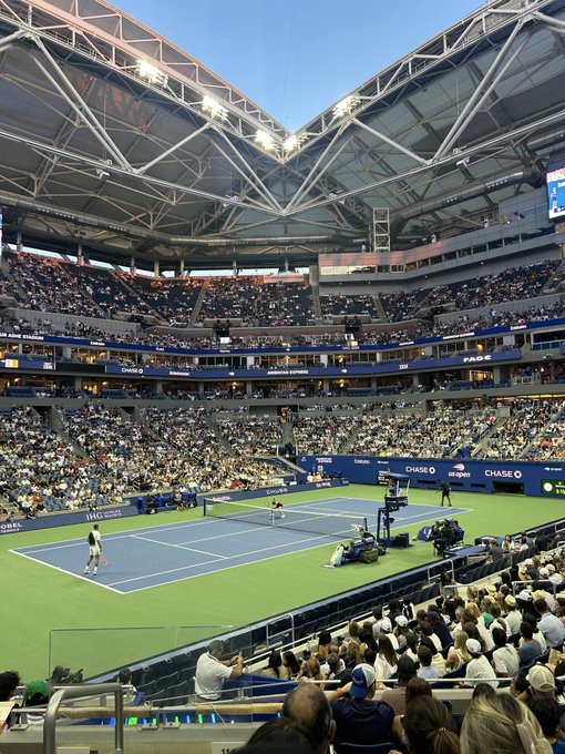 An interior view of Arthur Ashe Stadium at the US Open tennis tournament, showing a match in progress with 'CHASE' sponsor signage visible.