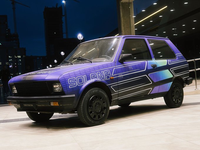 A purple and blue hatchback car with 'SOLANA' branding displayed in a modern indoor venue at night.