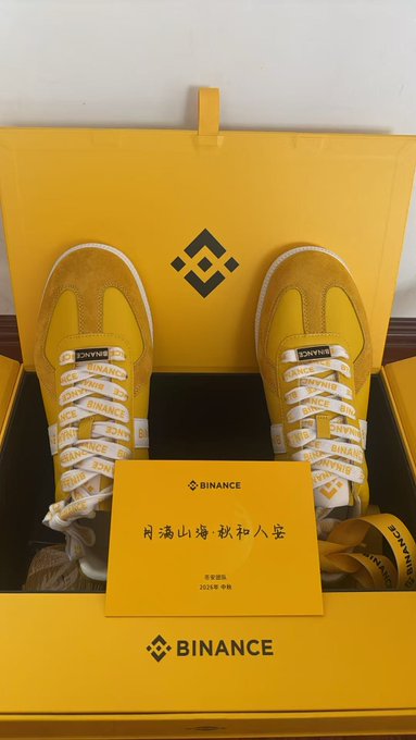 A pair of yellow Binance-branded sneakers with branded laces sits inside a yellow Binance shoebox, accompanied by a Binance-branded card with Chinese characters.