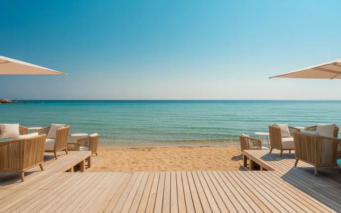 The image shows a beautiful beach scene, featuring two white umbrellas providing shade over several chairs and tables. The chairs are arranged under the umbrellas, offering a comfortable spot for relaxation. In addition to the seating area, there's also a bench nearby. The beach is located near the ocean, with its vast expanse of water stretching out towards the horizon. The sky above is clear blue, indicating pleasant weather conditions.