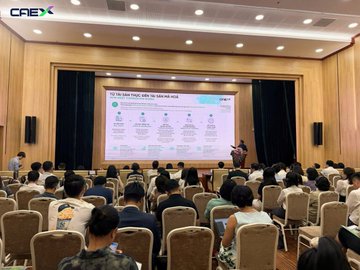 The image shows a large group of people sitting in chairs, watching a presentation by Chris Chiew. The audience appears engaged as they listen to him speak about the Vietnam Prosperous CAEX Cryptocurrency Exchange. The event takes place at a conference or market development orientation, and it is scheduled for June 5th, 2006.