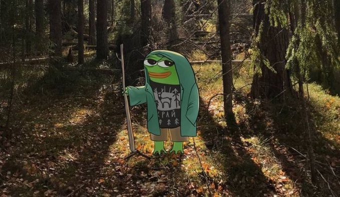 A Pepe the Frog character wearing a green hooded robe and a sweater with Cyrillic text stands in a forest holding a wooden staff.
