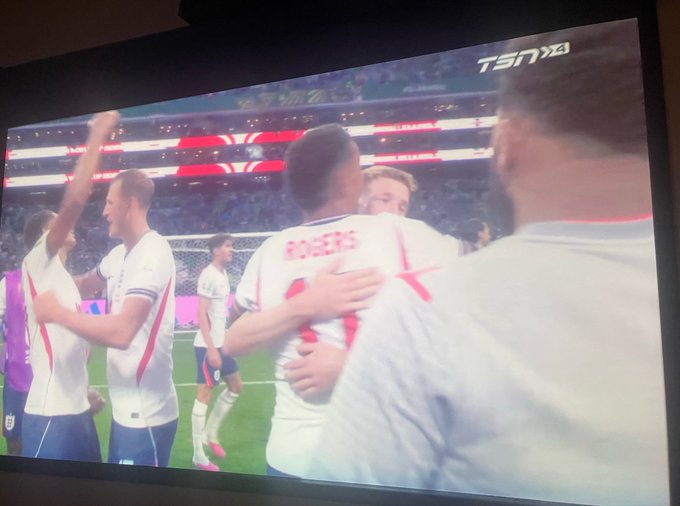 A photo of a TV screen displaying a TSN4 broadcast of soccer/football players in white jerseys (with 'ROGERS' visible on one) celebrating on the pitch in a stadium.