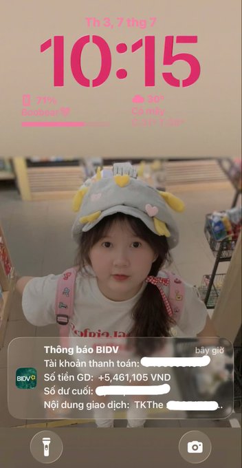A phone lock screen showing the time 10:15 on Thursday, July 3rd, with a photo of a child in a cute hat in the background. A BIDV bank notification displays a credit of +5,461,105 VND.