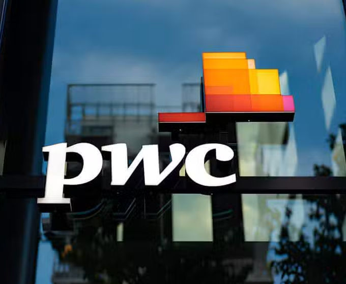 The image shows the illuminated "pwc" logo on a glass building exterior, featuring the firm's signature multicolored pixelated design in orange, red, and yellow hues against a dark background. The caption relates directly to the post, as PwC is the professional services firm providing analysis on proposed U.S. Congressional tax policies that would treat Bitcoin similarly to stocks while distinguishing stablecoins, mining rewards, and wash-sale rules.