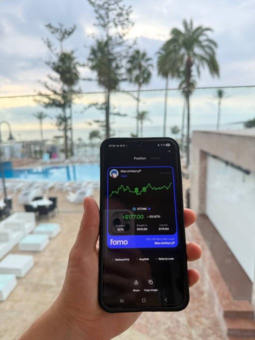 A hand holds a smartphone displaying the 'fomo' app with a stock price graph for 'MarvinIsJerry' currently at $177.00, with a resort pool and palm trees visible in the background.