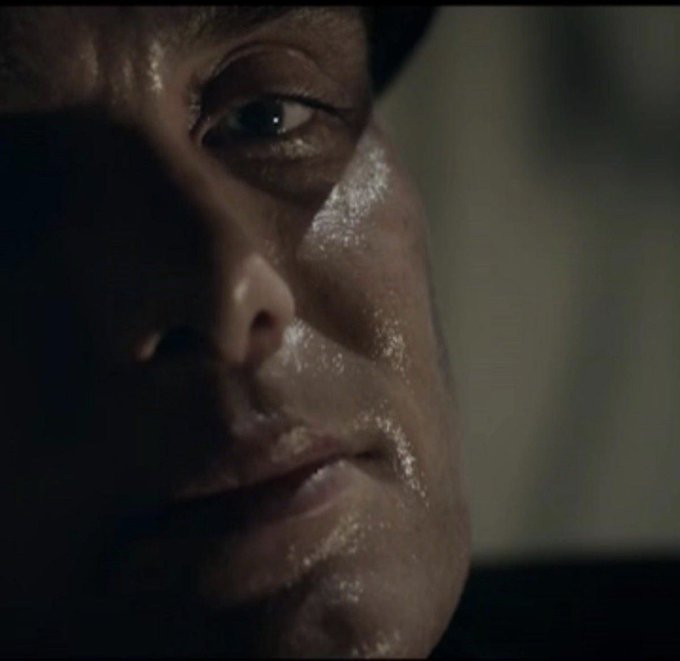 A close-up of a sweaty man's face in dim lighting, with his intense gaze directed to the side, showing visible moisture and reflections on his skin.