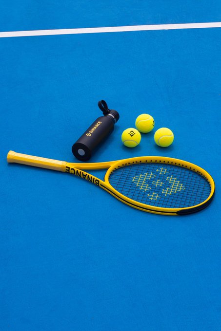 A yellow Bonming tennis racket and three tennis balls arranged on a blue tennis court alongside a black water bottle.
