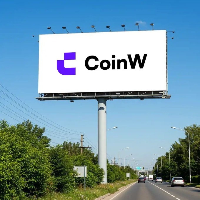 A large roadside billboard displays the "CoinW" logo with a purple "W" icon against a white background, towering over a highway under a clear blue sky. The image visually reinforces the post's message about the "W" becoming increasingly prominent and difficult to overlook, as the brand's signage now takes center stage in a high-traffic public space.
