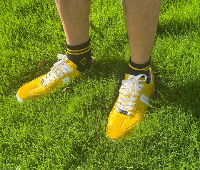 A person wearing bright yellow athletic shoes with white laces and black-and-yellow striped socks stands on lush green grass.