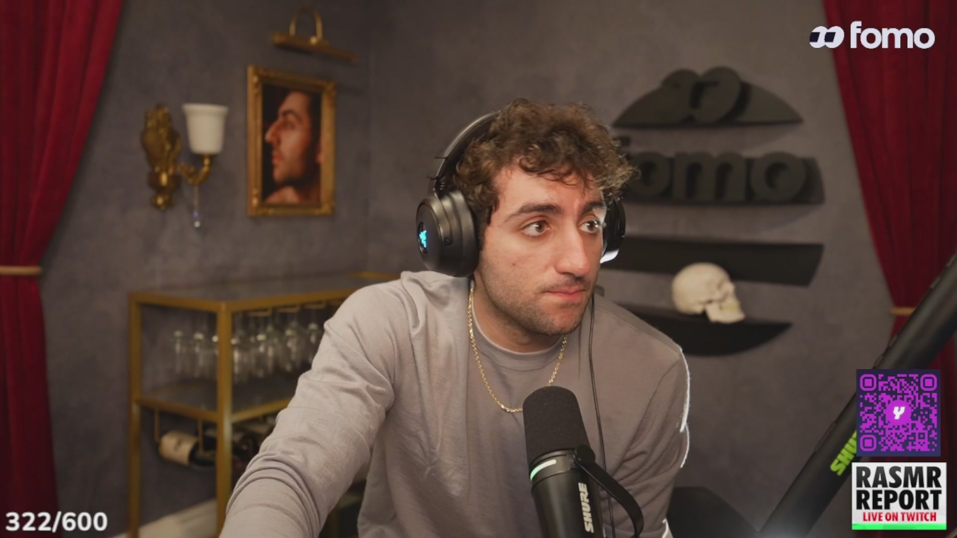 urns of water, wine glasses, and a portrait adorn the walls of a dimly lit room with a man wearing headphones seated at a microphone.