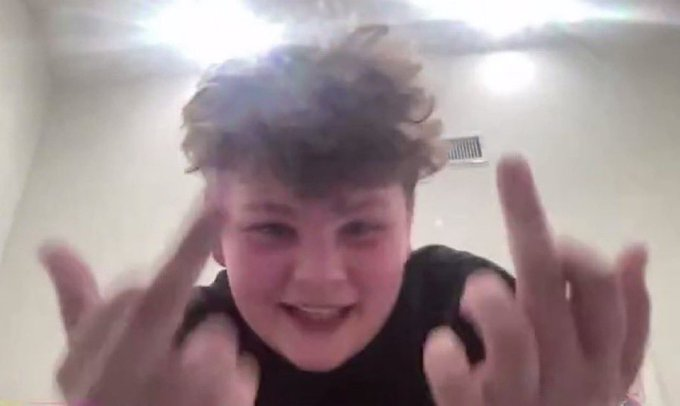 A young person with curly hair makes rock-on hand gestures toward the camera with a bright lens flare overhead.