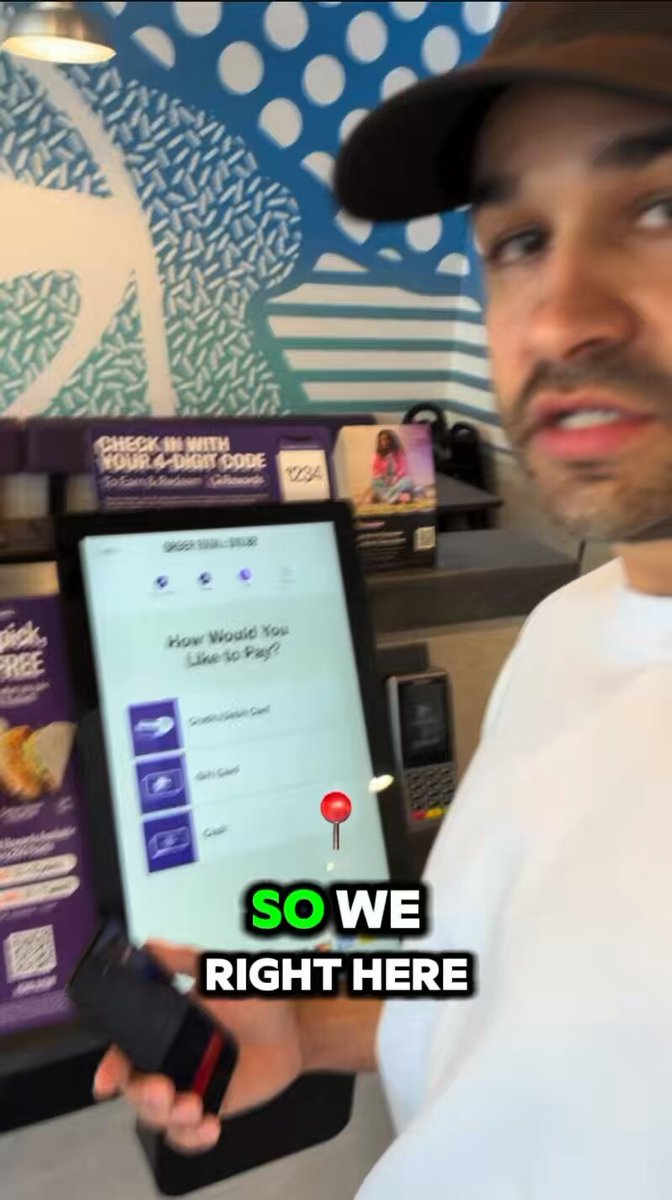 The image features a man holding up an electronic device that appears to be a tablet or e-reader. The device has a screen displaying "So We Right Here", which could possibly be a prompt for a payment system, such as Tangem Pay. The man is wearing a hat and a white shirt, giving him a casual appearance.