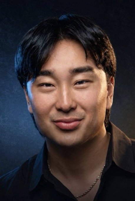 A man with dark hair smiles softly in a professional portrait against a moody blue background, wearing a dark shirt and a thin chain necklace. The post frames him as the "Founder of PUMPFUN" in a comparison to a rival crypto/meme coin founder.