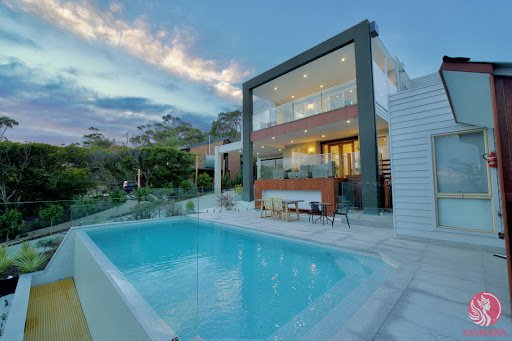 Caption: "This aesthetic home features a bright blue pool adjacent to a modern house with large floor-to-ceiling windows. The post accompanying this image highlights an opportunity for builders to collaborate with @CNPYNetwork, presumably relating to the innovative design elements of the house."
