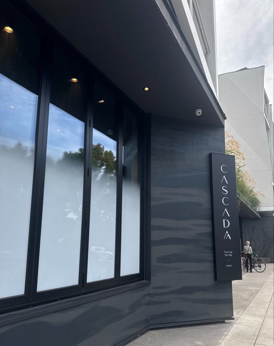 The exterior corner of a modern dark-painted building featuring a vertical 'CASCADA' sign listing services like Thermal, Springs, and Hotel.