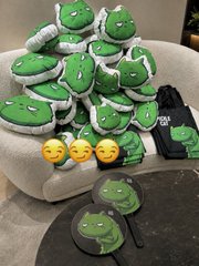 A collection of green dinosaur-themed merchandise including plush toys, slippers, and emoji cushions arranged on a chair and table.