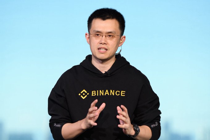 A man with glasses, appearing to be CZ (Changpeng Zhao), speaks while wearing a black "BINANCE" branded hoodie, gesturing with both hands. The image aligns with the post's caption as CZ, Binance's founder, is shown addressing an audience in a setting that suggests a discussion about market optimism.
