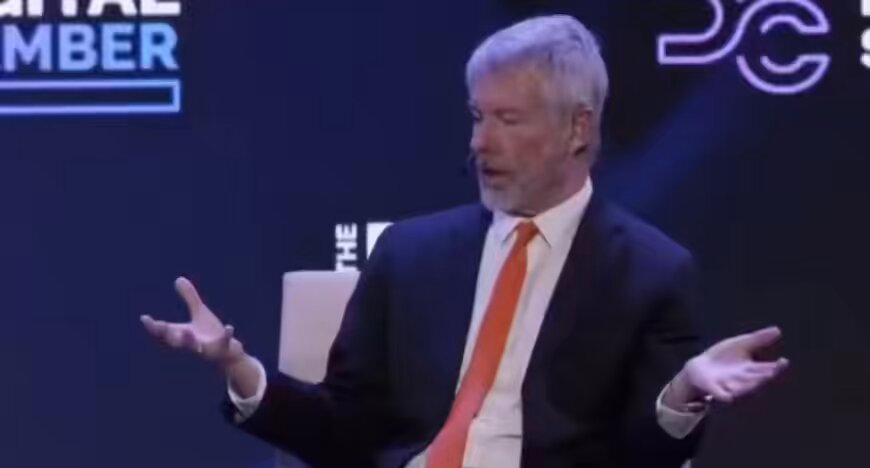 The image shows a man wearing a suit and tie with his arms outstretched as if he's trying to emphasize something or make a statement. The man appears to be delivering a speech, possibly at an event related to Bitcoin. At the bottom of the image, there is text that reads "MICHAEL SAYLOR SAID BITCOIN IS GOING TO $50,000,000 TIGHTEN YOUR SEATBELTS". This message suggests that the discussion or situation in the photograph might be connected to the value and potential impact of Bitcoin on people's finances.