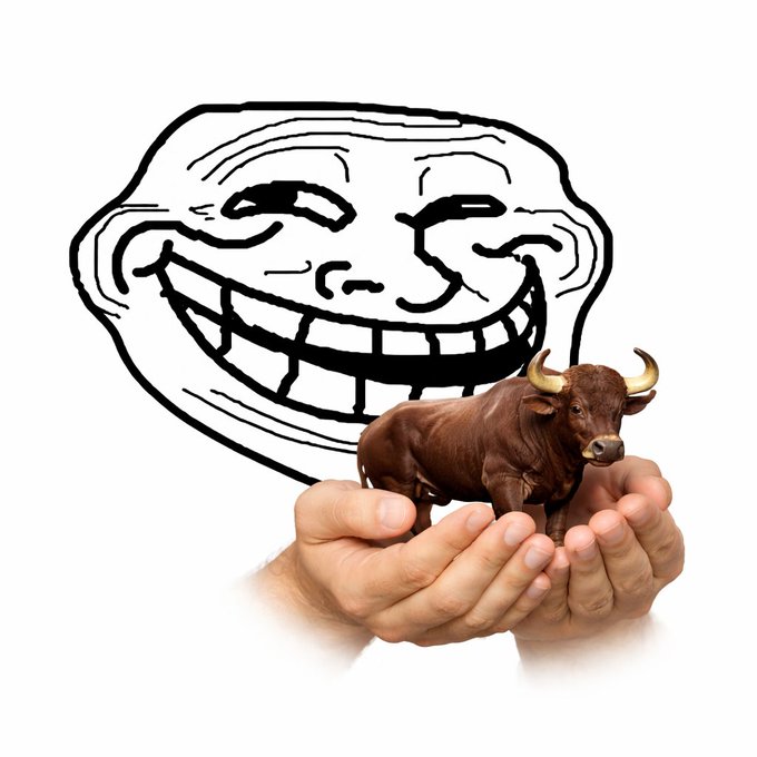 A troll face meme illustration behind a pair of hands cradling a small brown bull figurine with golden horns.