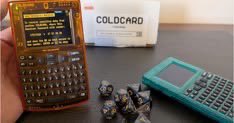 A close-up of a red Coldcard Mk4 hardware wallet displaying a QR code, sitting on a desk next to its box and a teal calculator device.