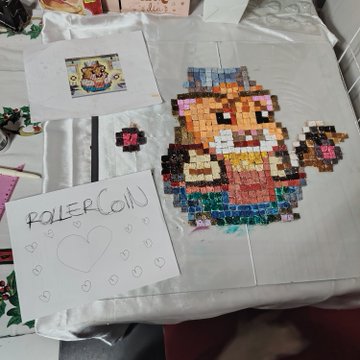 A handmade display featuring a pixel art mosaic of a character from a video game (appearing to be from Animal Crossing), accompanied by a drawing of a cat labeled 'ROLLERCON' and a small cat sticker.