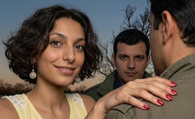 The image shows a smiling woman with curly hair and dangling earrings placing her hand on a man's shoulder, while another man in the background glares at him—capturing a classic love triangle moment. It pairs with the meme as a humorous metaphor for the jealousy and betrayal of chasing meme coin hype, only to watch someone else profit while you're left holding the bag.
