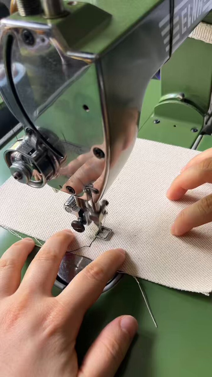 The image shows a person's hands operating a sewing machine with a green body and silver accents. The person is holding the fabric under the needle of the sewing machine while they work on a project, possibly making clothes or other textile items. The background appears to be a green surface, which could be a table or a workspace for the sewing process. The image also contains text that reads "A documentary about the making of the Sewunter-Strike game. Last 4 editions, 30 xtz." This suggests that there might be a connection between the person's sewing activity and the production of the video game, Sewunter- Strike.