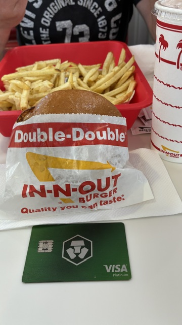 The image shows a meal consisting of a burger, fries, and a drink at a fast food restaurant. The meal appears to be quick and tasty but may not be the healthiest option. A green Visa card is placed next to the meal on the table, suggesting that the person who ordered this meal might have used their Visa credit card for payment.