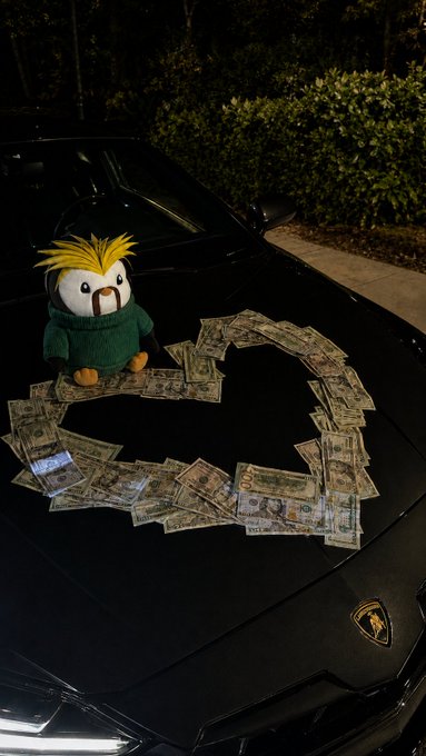 A plush penguin toy with yellow spiky hair and a green sweater sitting on the hood of a black Lamborghini, surrounded by a heart-shaped arrangement of US dollar bills.