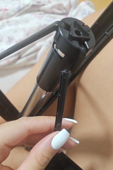 A close-up shows a hand with white painted nails holding a black plastic component, possibly part of a tripod or stand.