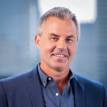 A professional headshot of Eric Balchunas, the Bloomberg ETF analyst referenced in the post, smiling warmly at the camera while wearing a blue blazer over a patterned blue button-down shirt against a softly blurred office background.