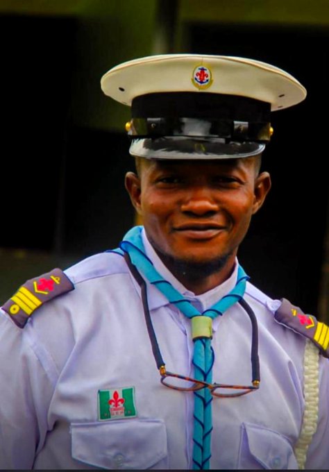 A portrait of a smiling man in a light purple uniform with shoulder epaulettes and a white peaked cap, with a pair of glasses hanging from his neckerchief.