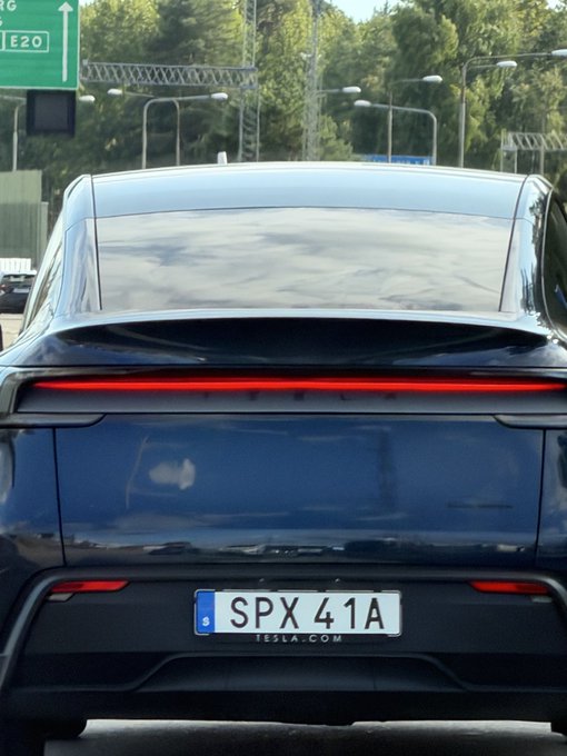 Rear view of a dark Tesla vehicle on a highway, displaying a Swedish license plate 'SPX 41A' with 'TESLA.COM' below it.
