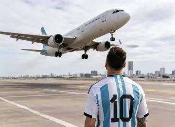 A person wearing an Argentina national team #10 soccer jersey (Messi) standing on a tarmac watching a commercial airplane fly overhead.