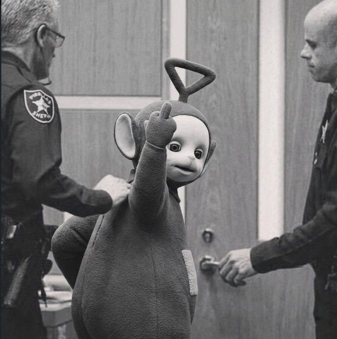 A vintage Teletubbies character Tinky Winky gives a middle finger while being held by a person wearing a sheriff's patch, with another man opening a door in the background, capturing the irreverent $ANSEM meme aesthetic.