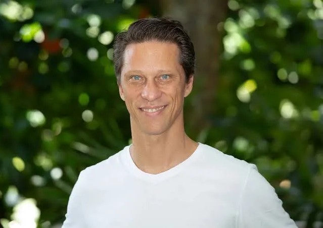 The image shows a smiling man with short brown hair and blue eyes wearing a white t-shirt, photographed outdoors against a backdrop of lush green foliage. This appears to be Raphael Zagury, CEO of Twenty One Capital ($XXI), who is quoted in the accompanying post about building a Bitcoin-backed Berkshire Hathaway-style company.