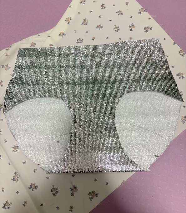 A pair of silver metallic underwear shorts laid out on a floral fabric background.