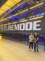 Two people pose in front of a brightly lit yellow tunnel with signage reading 'FUTUREMODE'.