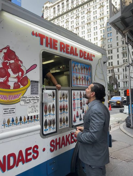 A man in a gray suit orders at an ice cream truck labeled "THE REAL DEAL," with visible sundae and shake menu listings including a "WATER $2.75" sign and credit card acceptance notice. The "Real Deal" branding ties into the post's play on words questioning whether the company's advertised offerings live up to its name.