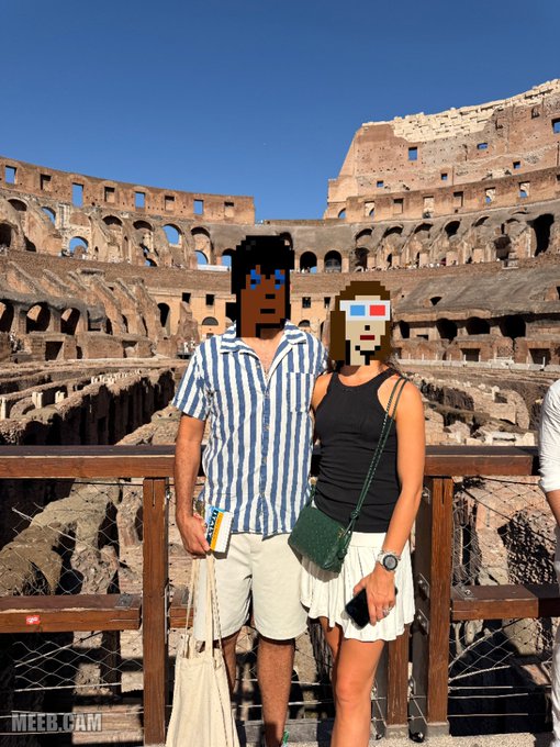 A couple poses for a photo at the Colosseum in Rome, with their faces pixelated with meme-style emoticons; the man wears a blue and white striped shirt and the woman wears a black tank top and white skirt, with a 'MEEB.CAM' watermark visible.