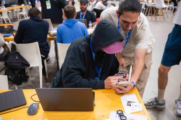 In this image from ETHGlobal Lisbon, two participants are intensely focused on their devices, likely finalizing project submissions for the upcoming judging rounds. The scene depicts the collaborative and driven atmosphere of a hackathon as participants prepare for the final push.