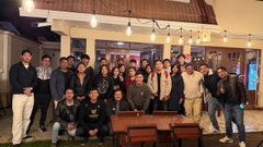 A group photo of approximately twenty people gathered indoors at what appears to be a restaurant or lounge, posing together for the camera.