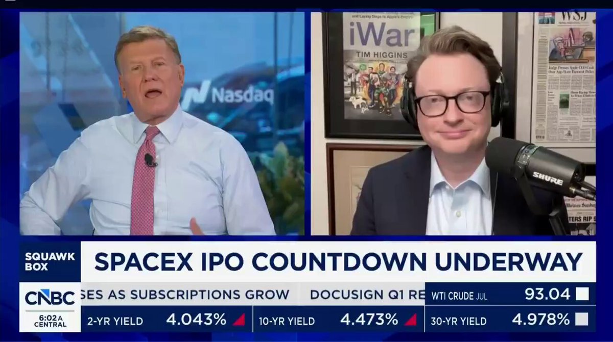 The image shows a news broadcast featuring two men talking about space exploration, specifically related to stock speculation. One man is wearing glasses and speaking into a microphone, while the other man is wearing a suit and tie. The TV screen displays a countdown of $1 trillion dollars that could potentially be invested in space companies like SpaceX by investors who want to capitalize on future space developments.