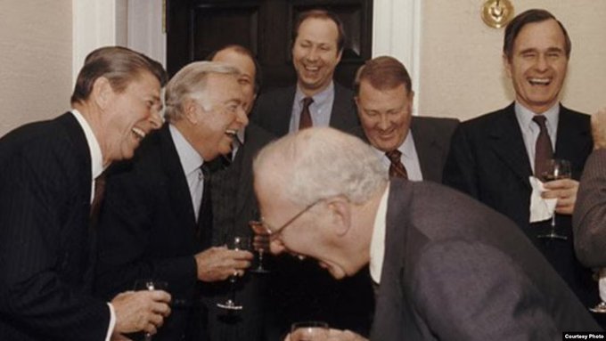 A historic color photograph of several politicians including Ronald Reagan laughing together at an indoor gathering, with a 'Courtesy Photo' watermark.