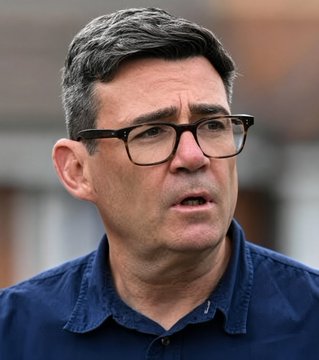 Portrait of a man with dark hair, wearing black-rimmed glasses and a dark blue shirt, looking slightly off-camera.