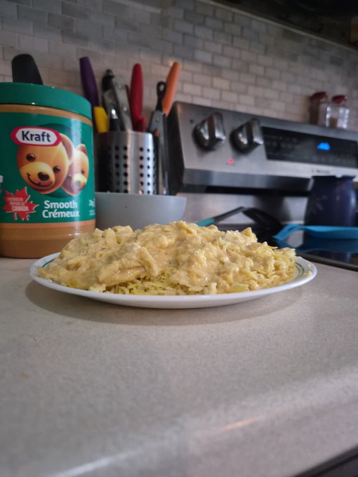 A plate of scrambled eggs sits on a kitchen counter, with a jar of Kraft Smooth Peanut Butter visible in the background alongside a utensil holder and stove.
