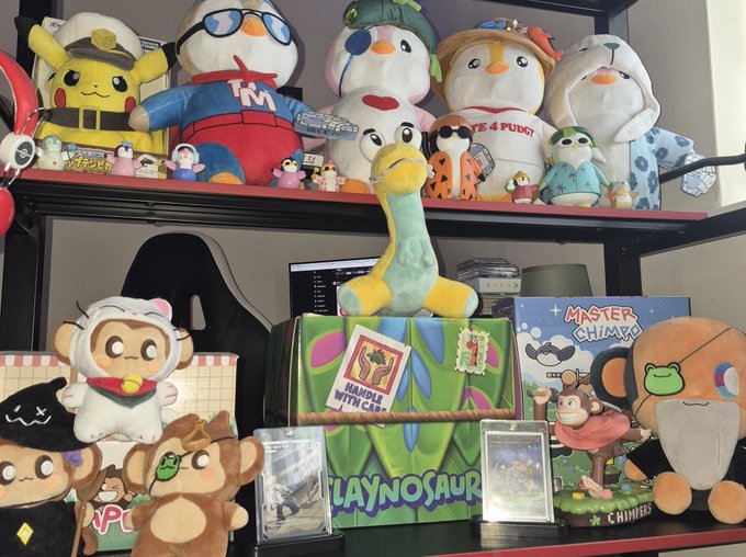 A shelf display of various plush toys and figurines, including a Pikachu, penguins, monkeys, a 'Playnosaur,' and a 'Master Chimp' board game.